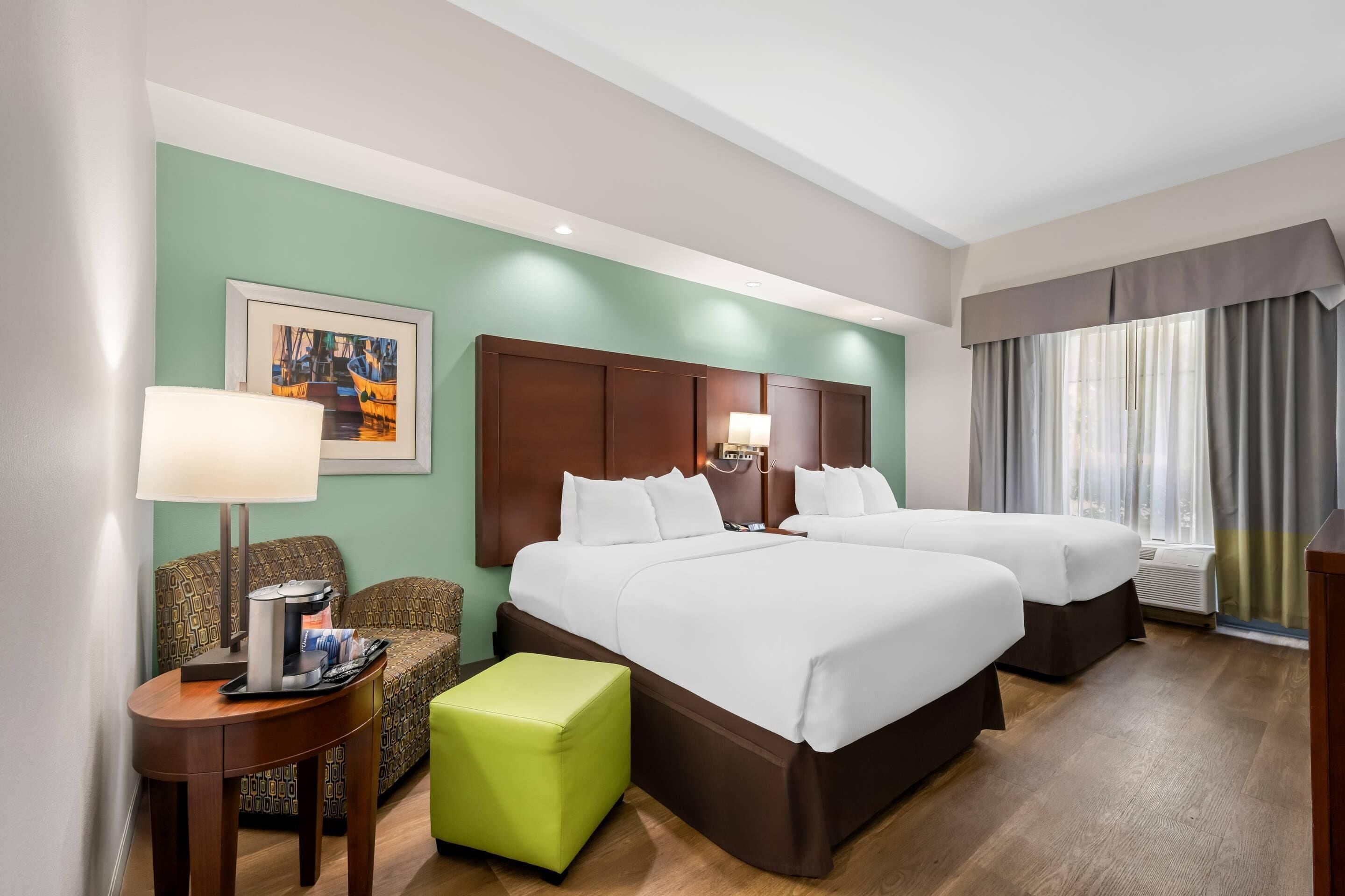 Habitación de hotel con dos camas, una pared verde, un cuadro enmarcado, una mesita de café y una ventana con cortinas.