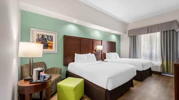 Habitación de hotel con dos camas, una pared verde, un cuadro enmarcado, una mesita de café y una ventana con cortinas.