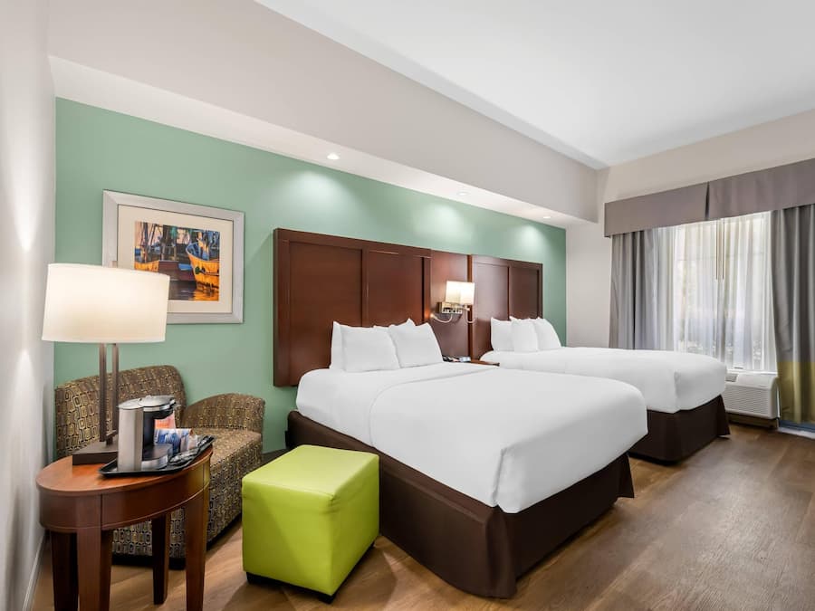 A hotel room with two beds, a green wall, a framed painting, a coffee table, and a window with curtains.