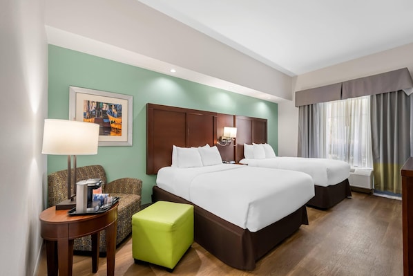 A hotel room with two beds, a green wall, a framed painting, a coffee table, and a window with curtains.