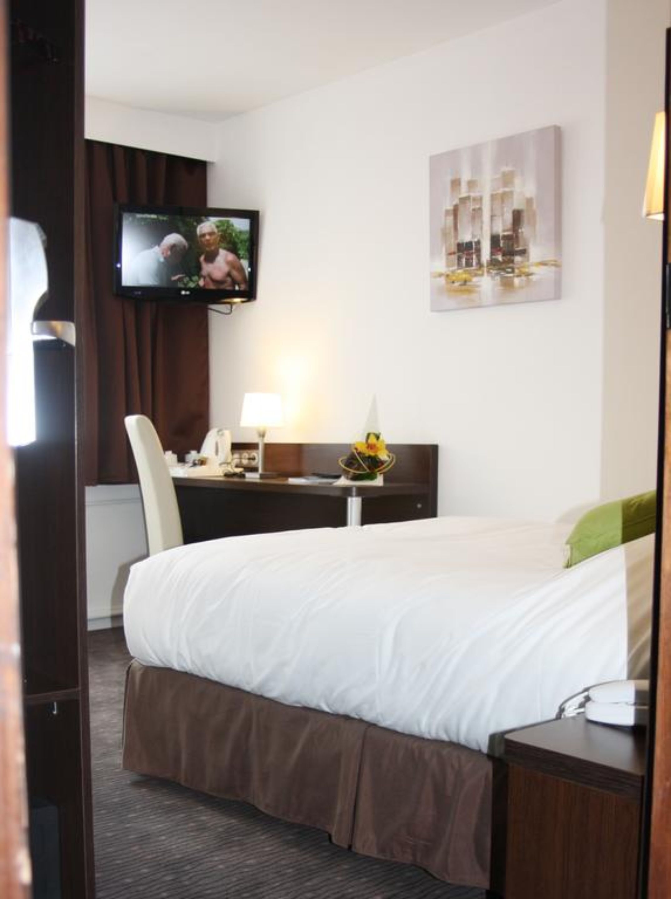 Een hotelkamer met een bed, een bureau met lamp, een televisie en kunst aan de muur.