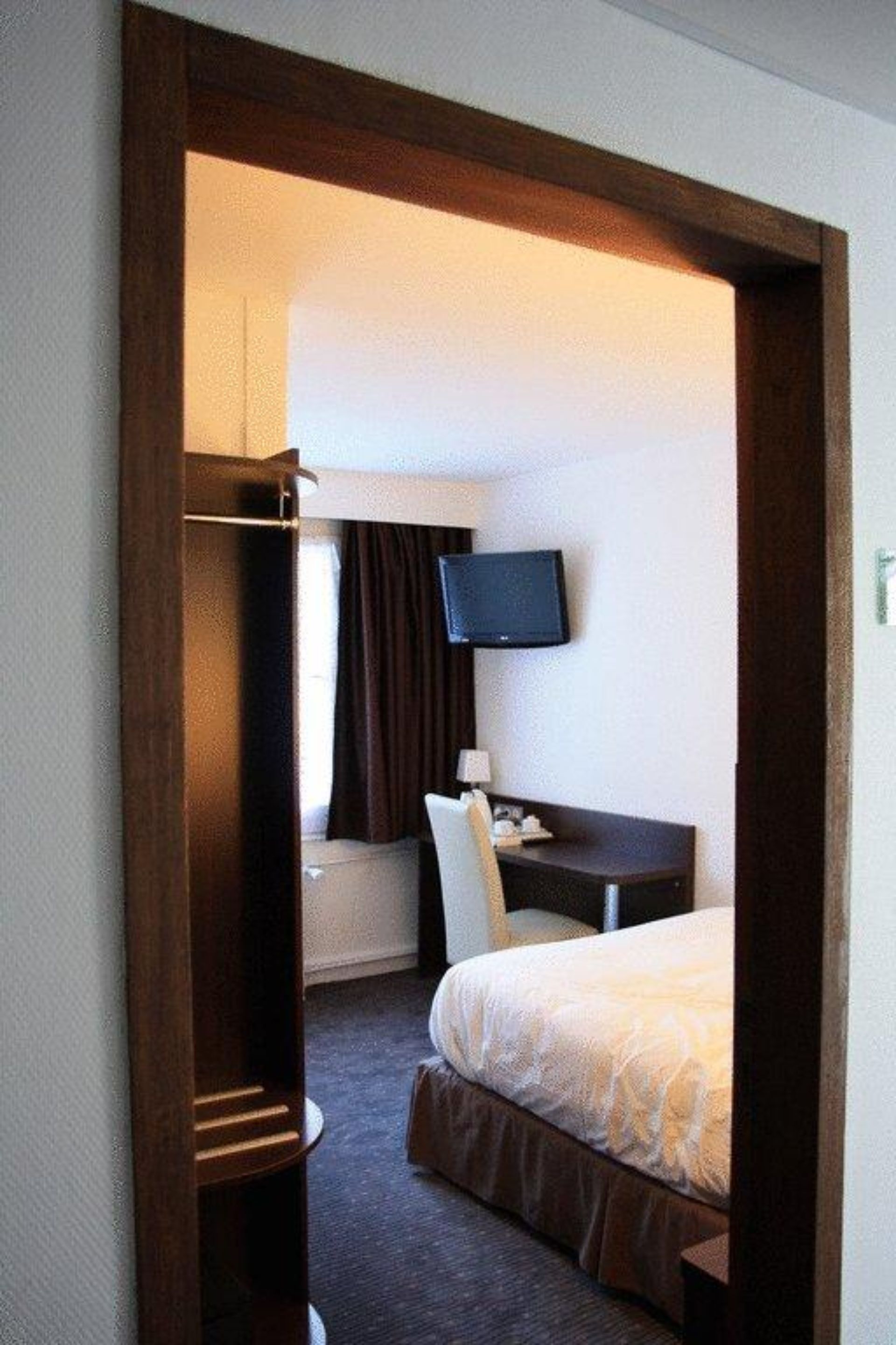 A hotel room with a bed, a desk, a television, and a wardrobe.