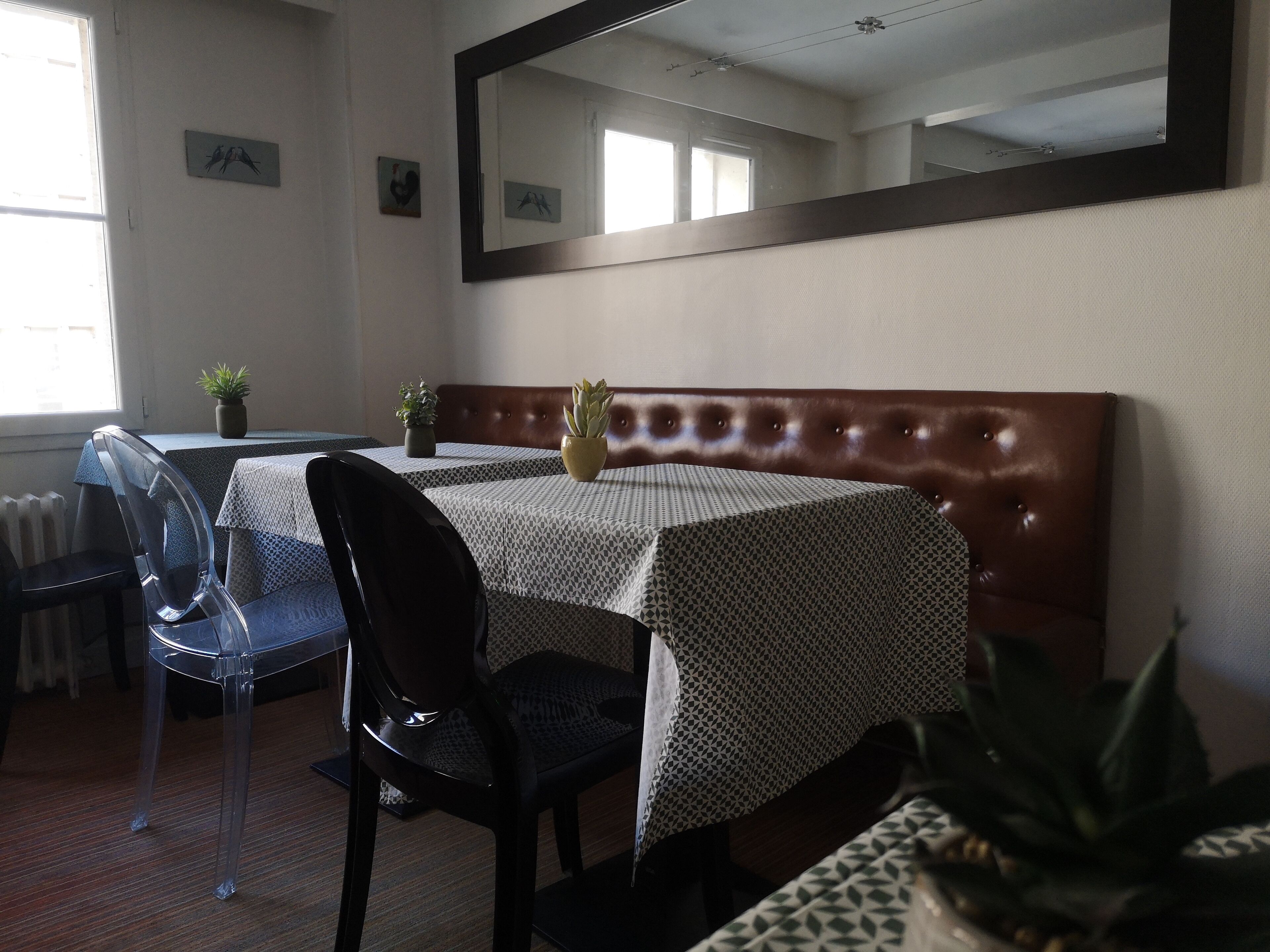 A hotel room with a dining table, chairs, a mirror, and a potted plant.