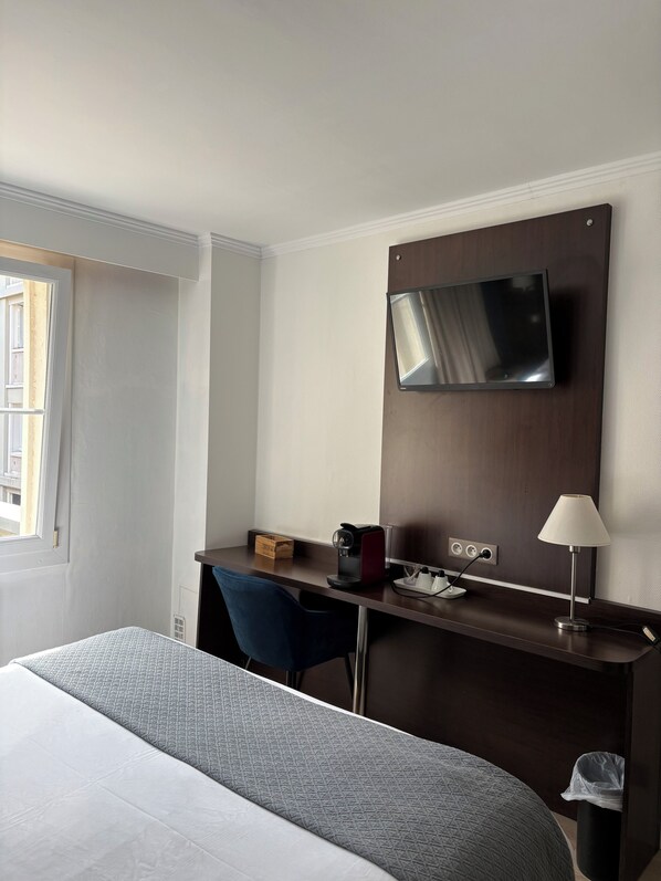 Habitación de hotel con cama, escritorio con silla, televisor montado en la pared y lámpara.