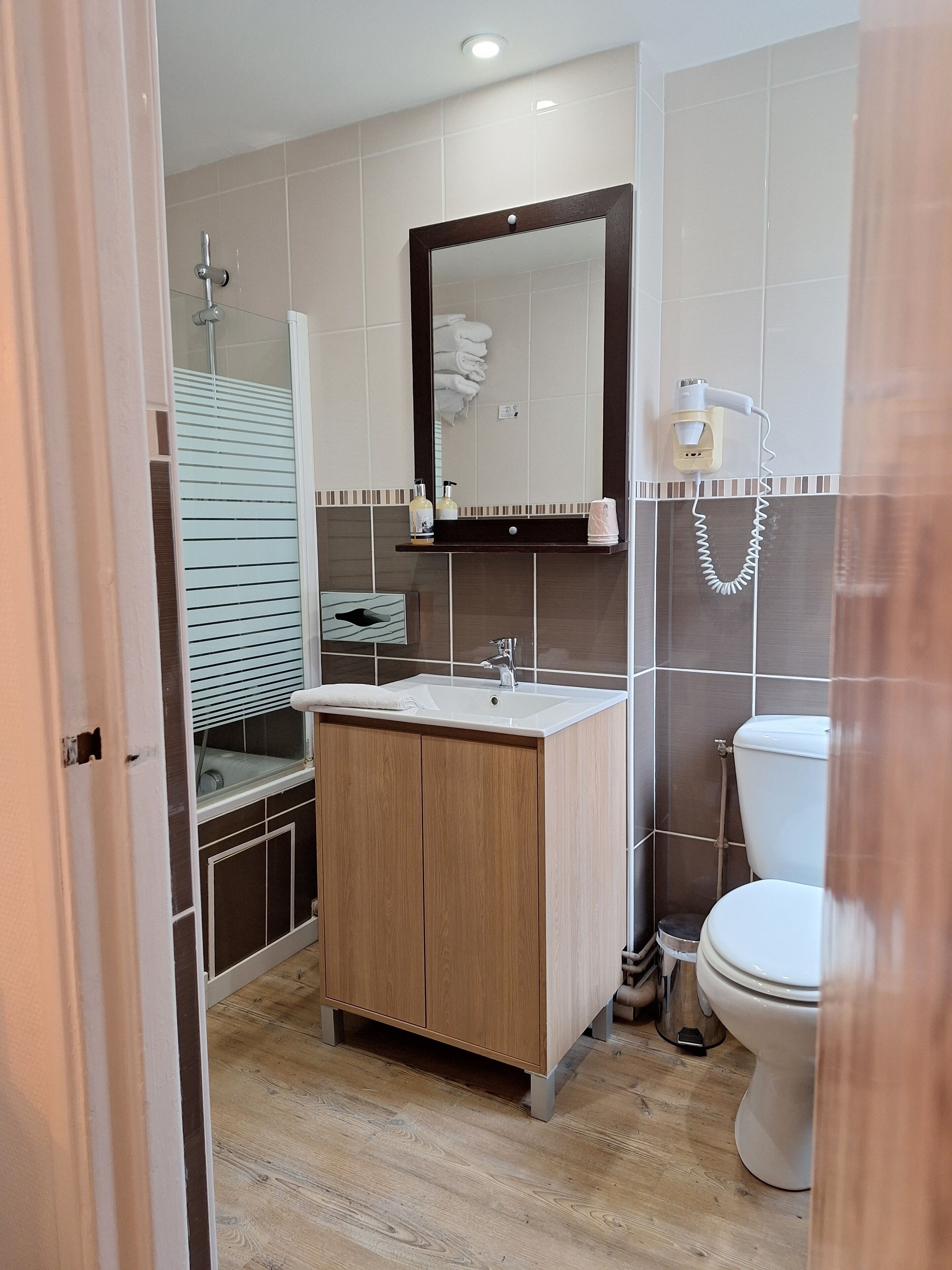A modern bathroom with a wooden vanity, a large mirror, a toilet, and a shower area.