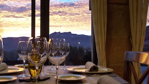 Une table dressée pour le dîner, avec des verres à vin et une bouteille, donnant sur un paysage montagneux au coucher du soleil.