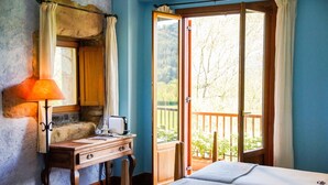 Une chambre à coucher avec un bureau en bois, une lampe, un lit et une grande fenêtre donnant sur des arbres.