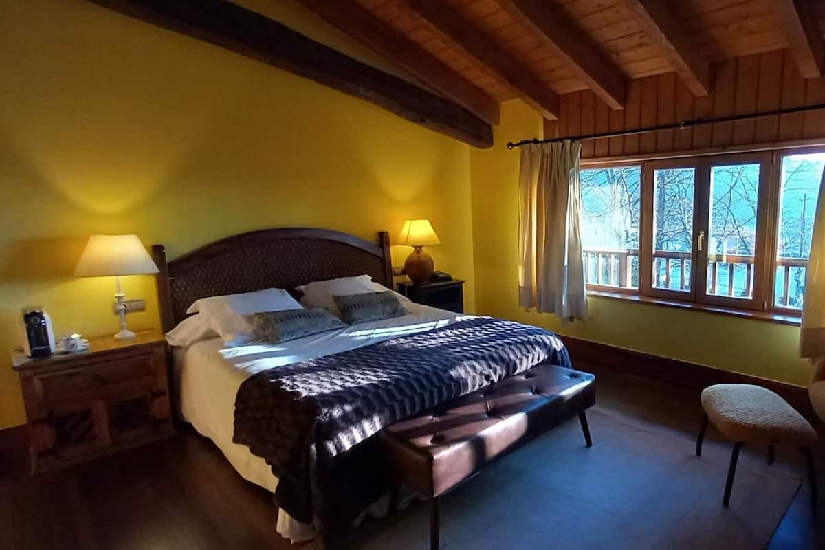 A bedroom with a wooden bed, two bedside lamps, a chair, and a window with curtains.