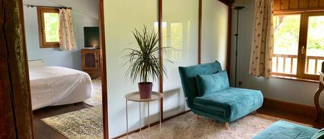 A room with a bed, a sofa, a potted plant, and a view of the outdoors.