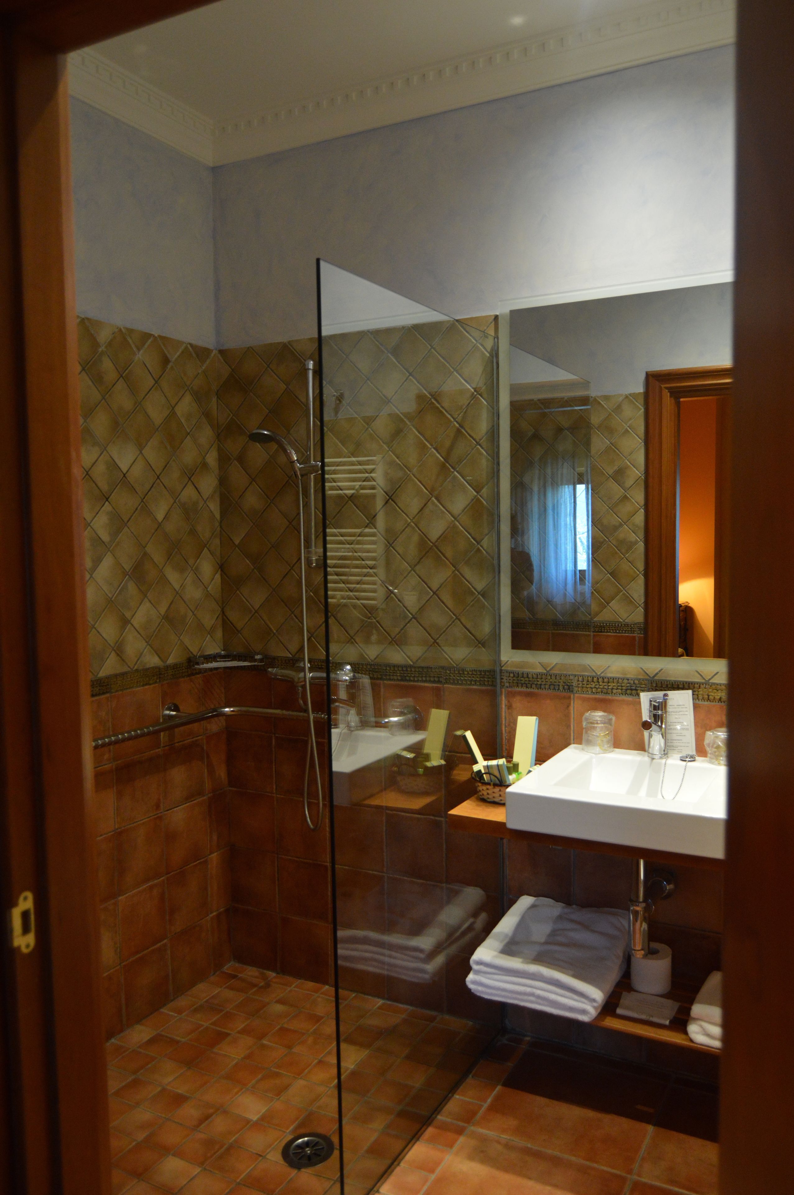 Ein Badezimmer mit einer Duschkabine, einem Waschbecken mit Toilettenartikeln und einem Spiegel, der den Raum widerspiegelt.