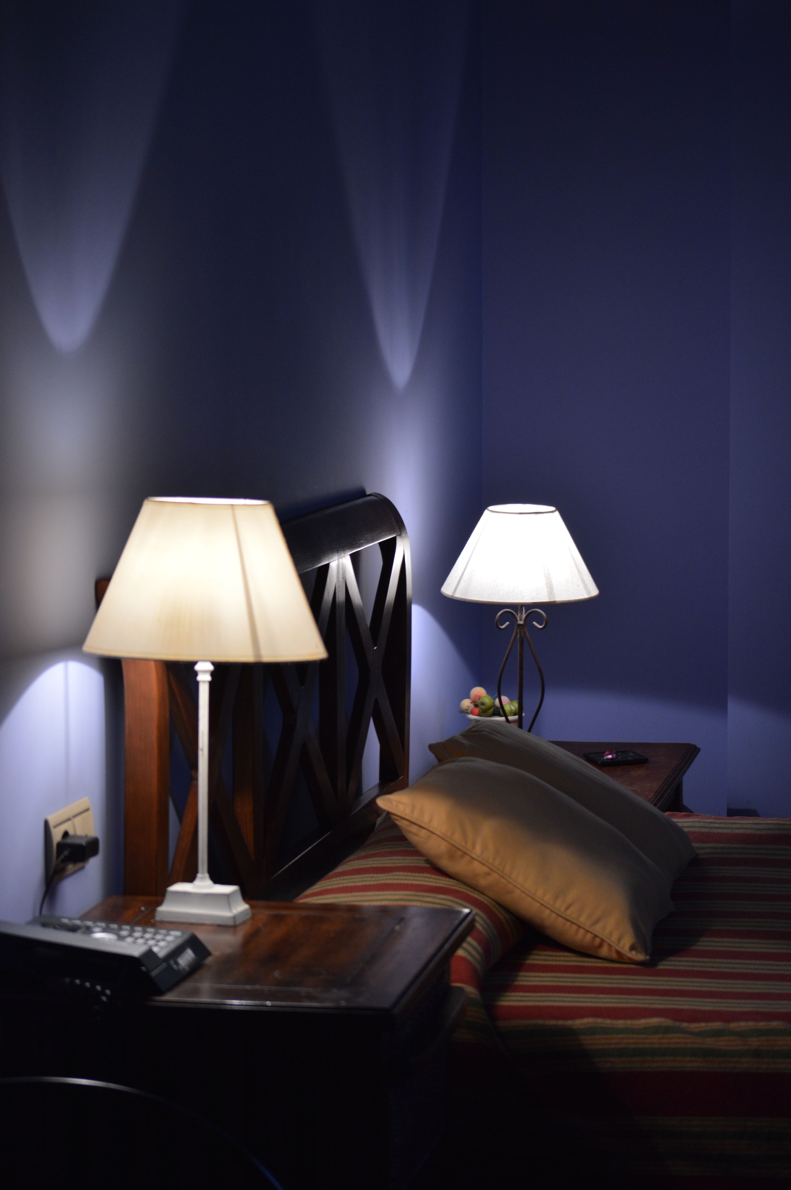 A hotel room with a bed, two bedside lamps, a wooden headboard, a nightstand with a remote control, and a pillow.
