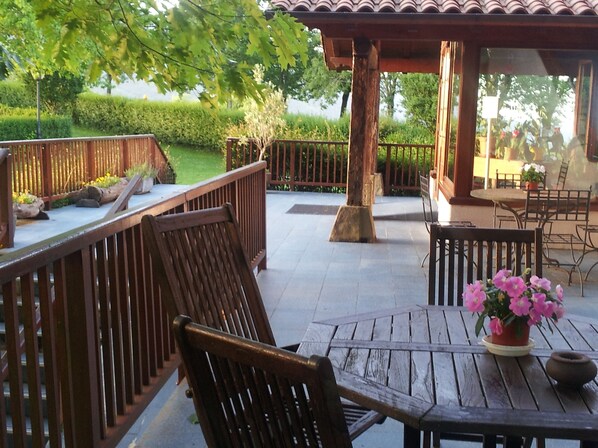 Un espace extérieur aménagé en terrasse, avec des meubles en bois, une pergola et une vue sur un jardin bien entretenu.