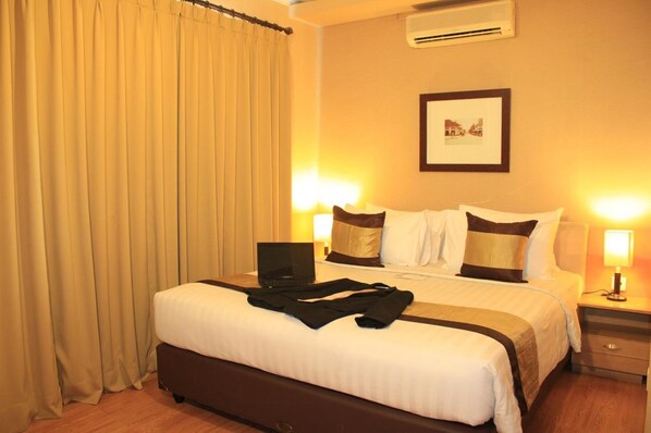 A hotel room with a bed, a laptop, and a nightstand with a lamp. - Grand Setiabudi Hotel (Bandung)
