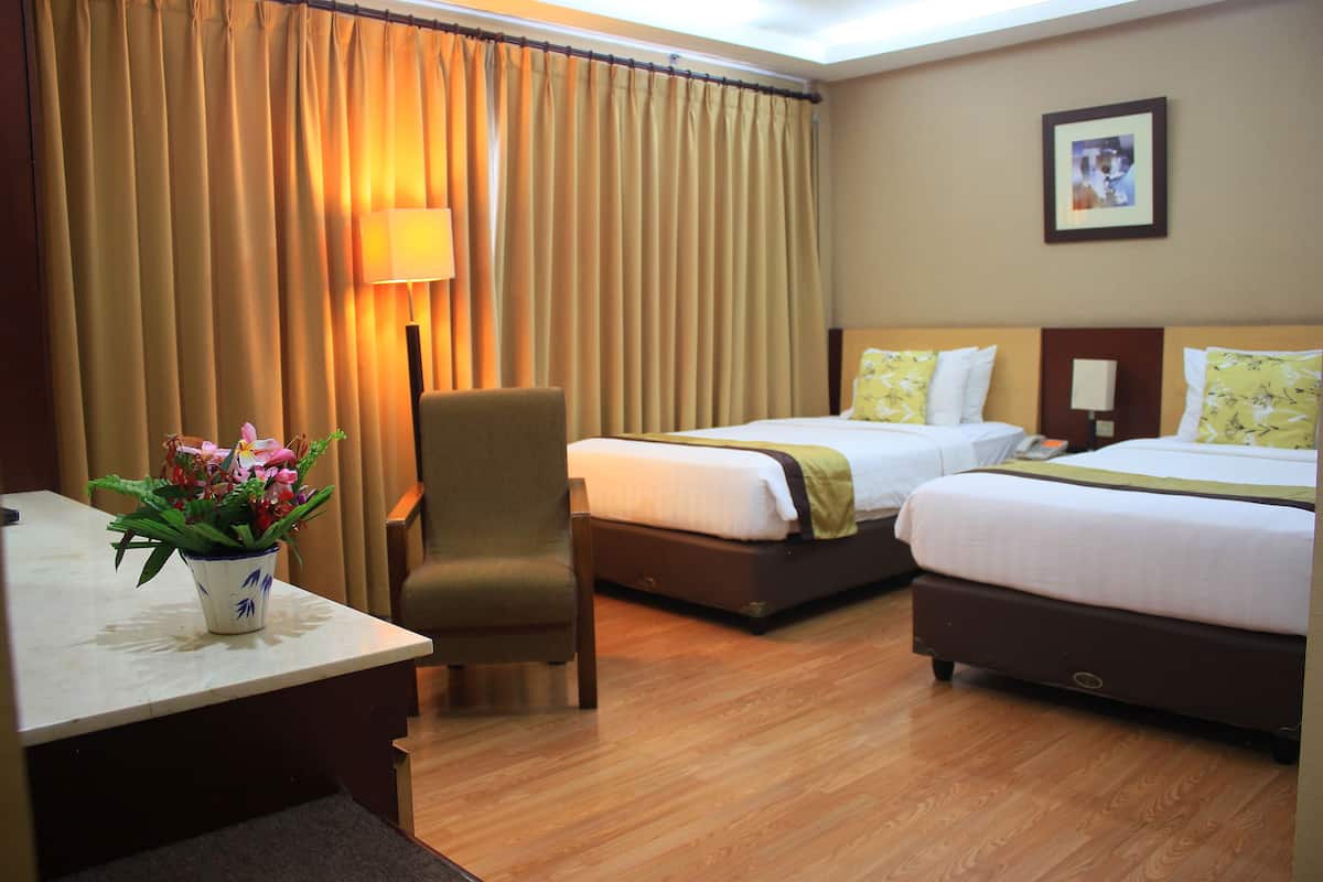 A hotel room with two beds, a desk, a chair, and a lamp.