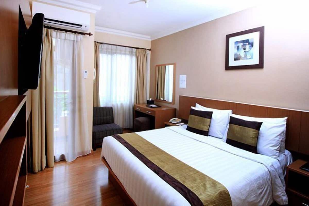 A hotel room with a bed, a desk, a chair, a TV, and a window with curtains.