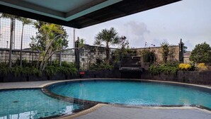 A swimming pool with a curved edge, surrounded by a stone wall and lush greenery. - Grand Setiabudi Hotel (Bandung)