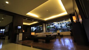 A modern interior with a large sectional sofa, a flat-screen TV, and a large window offering a view of the outdoors. - Grand Setiabudi Hotel (Bandung)