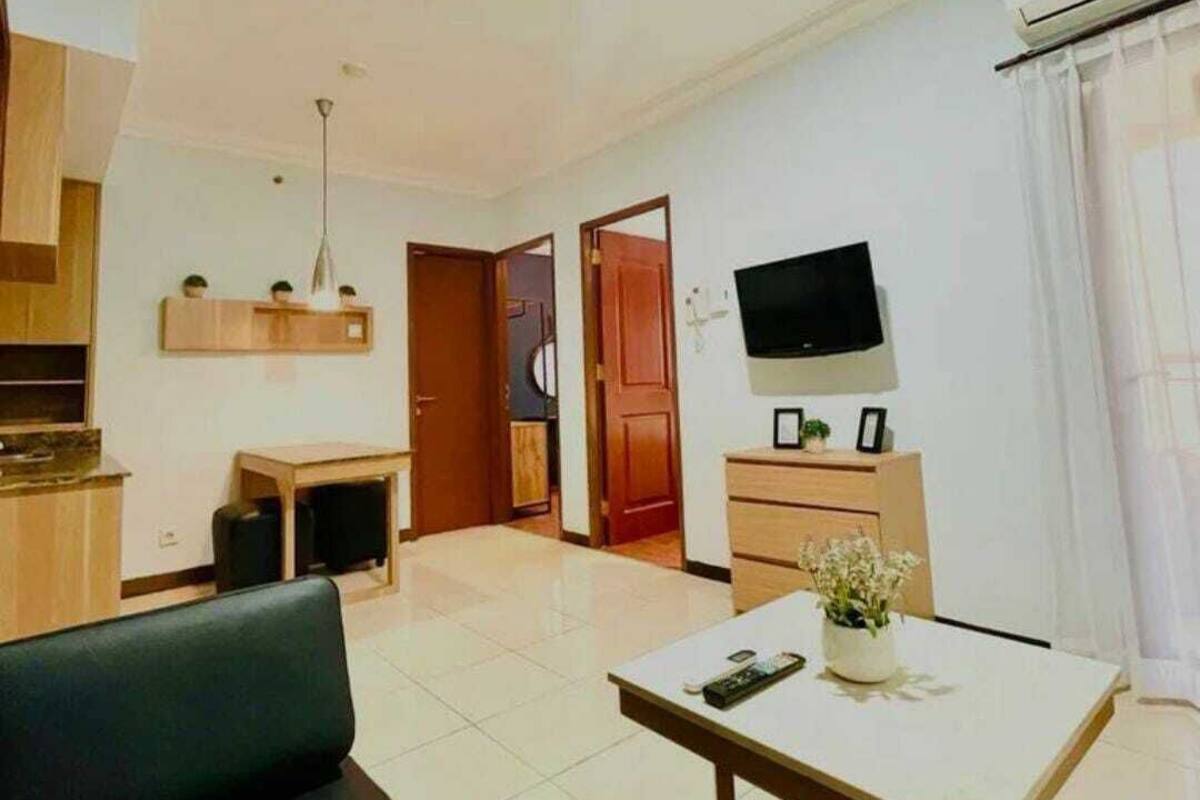 A modern living room with a sofa, a dining table, a TV, and a kitchen area with cabinets and a microwave.