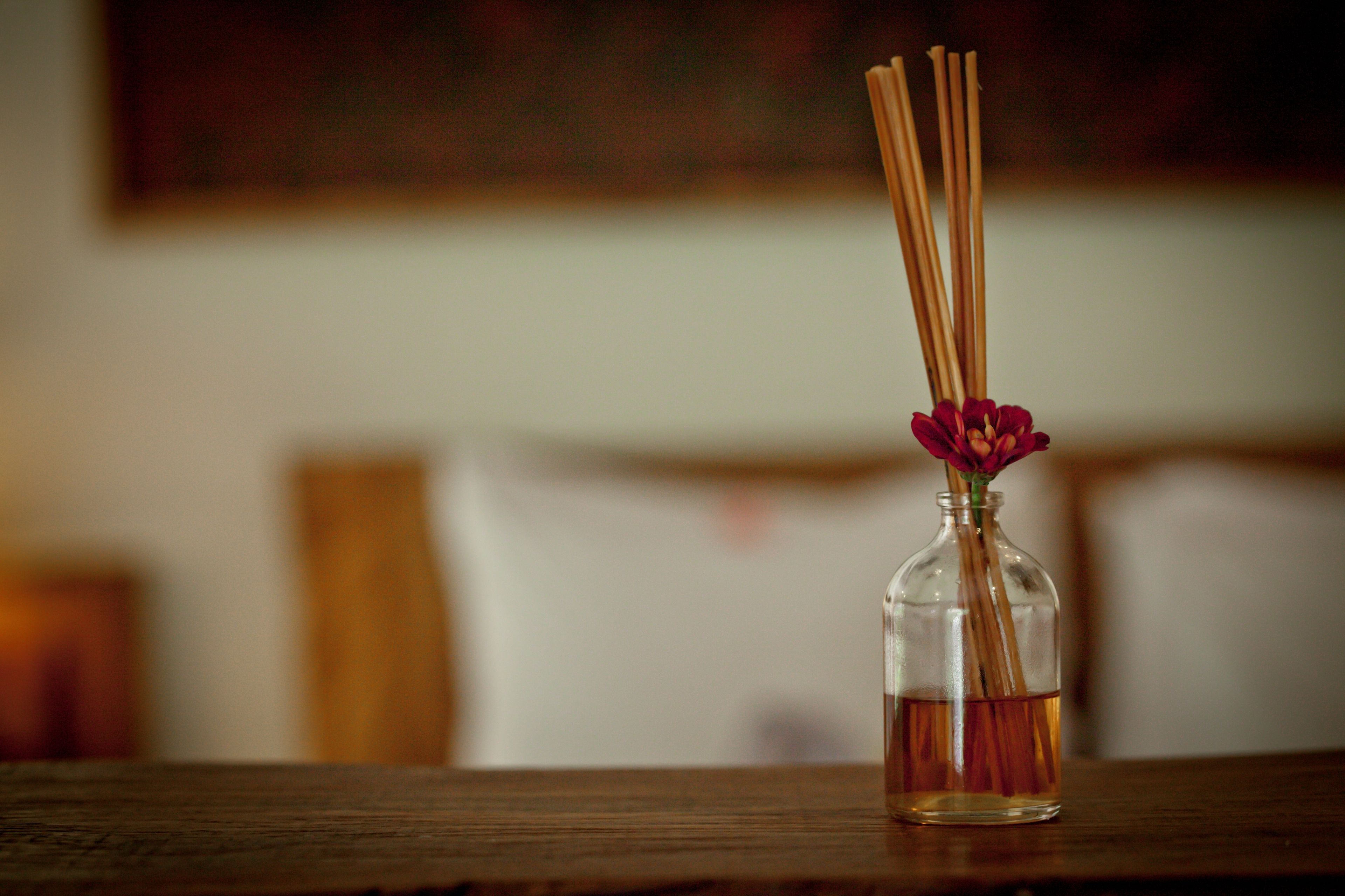 Una botella de vidrio transparente con una flor y ramitas sobre una superficie de madera.