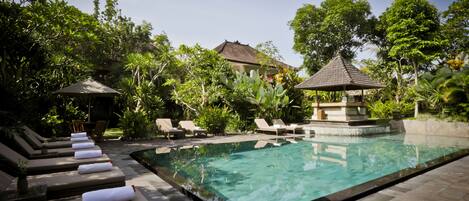 A swimming pool with lounge chairs and a gazebo, surrounded by lush greenery.