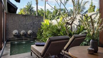 A pool area with a stone wall, a water feature, and lounge chairs.