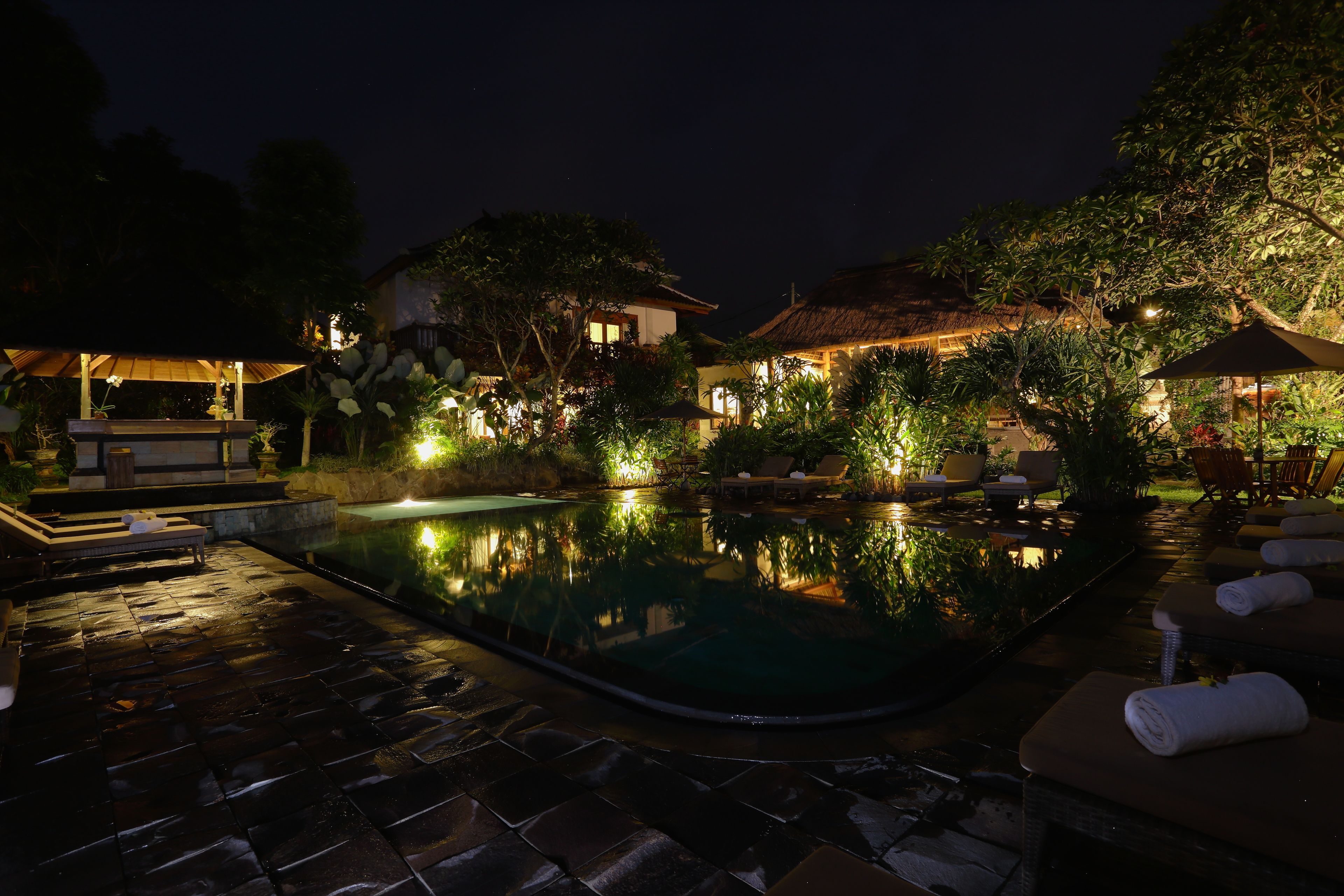 Area piscina notturna con sedie a sdraio e un gazebo.