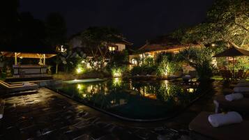 Area piscina notturna con sedie a sdraio e un gazebo.