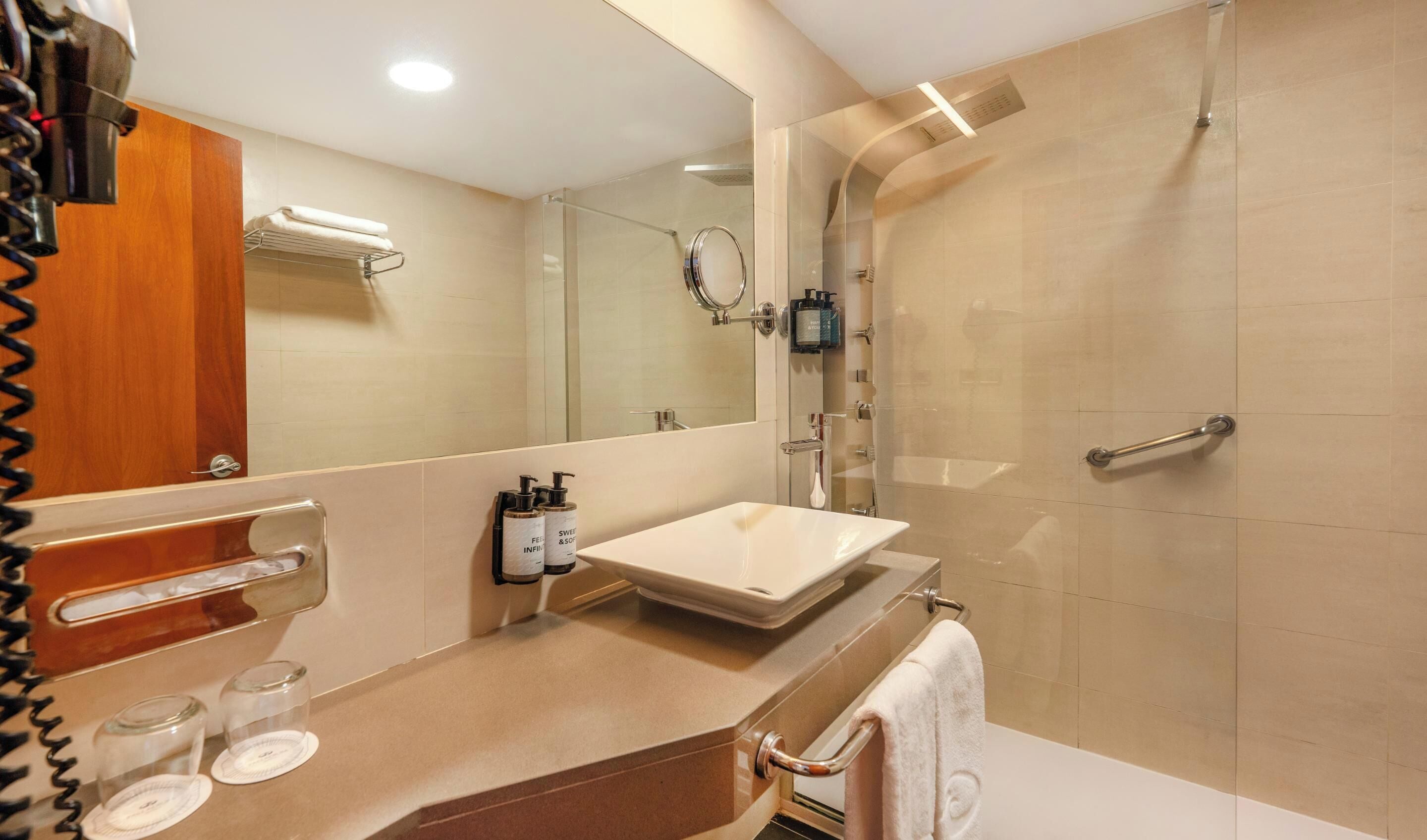 Un baño moderno con un espejo grande, un lavamanos y una zona de ducha.