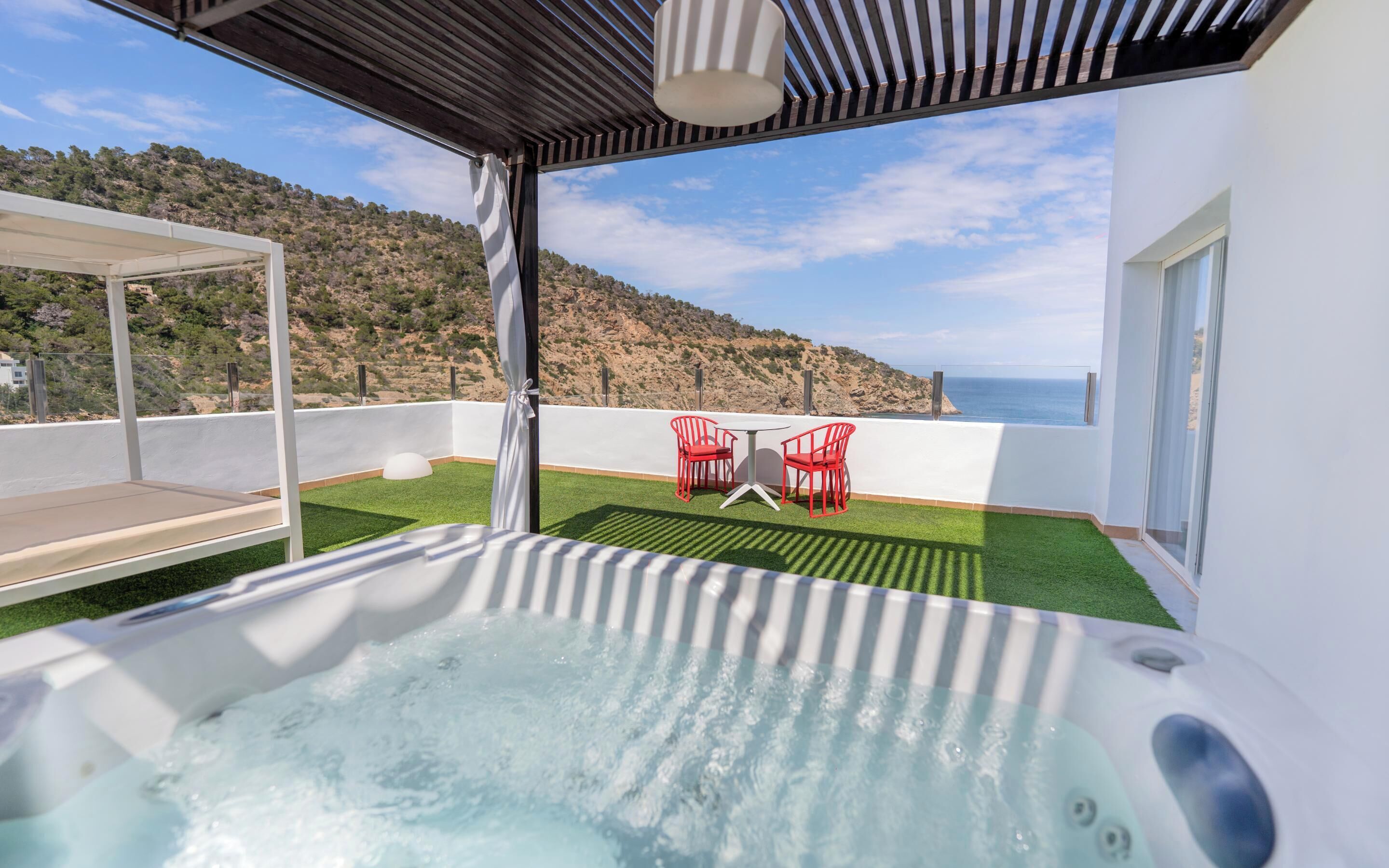 Een dakterras met een jacuzzi, rode stoelen en uitzicht op zee.