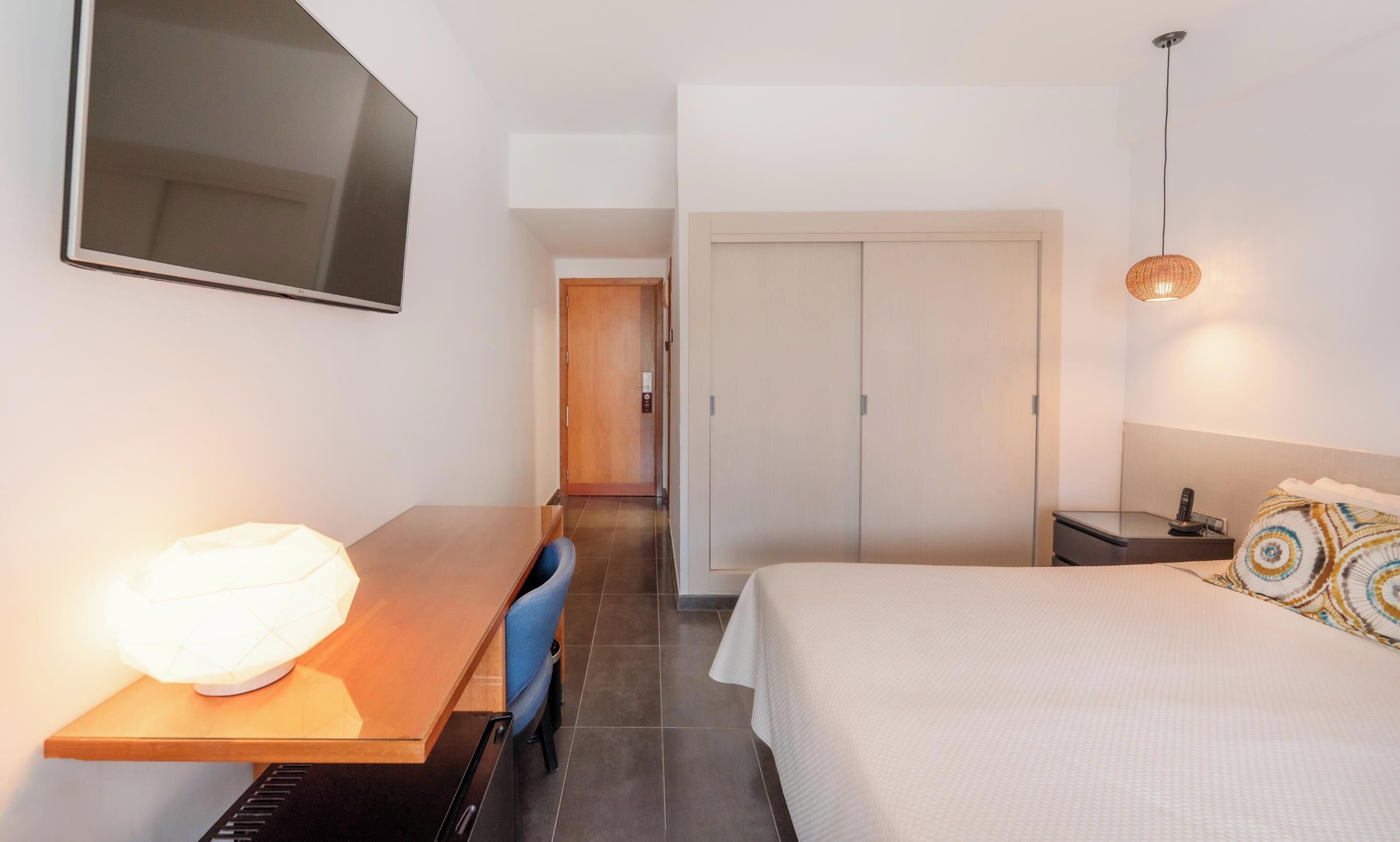 Een hotelkamer met een bed, een bureau met lamp, een stoel, een kledingkast en een televisie.
