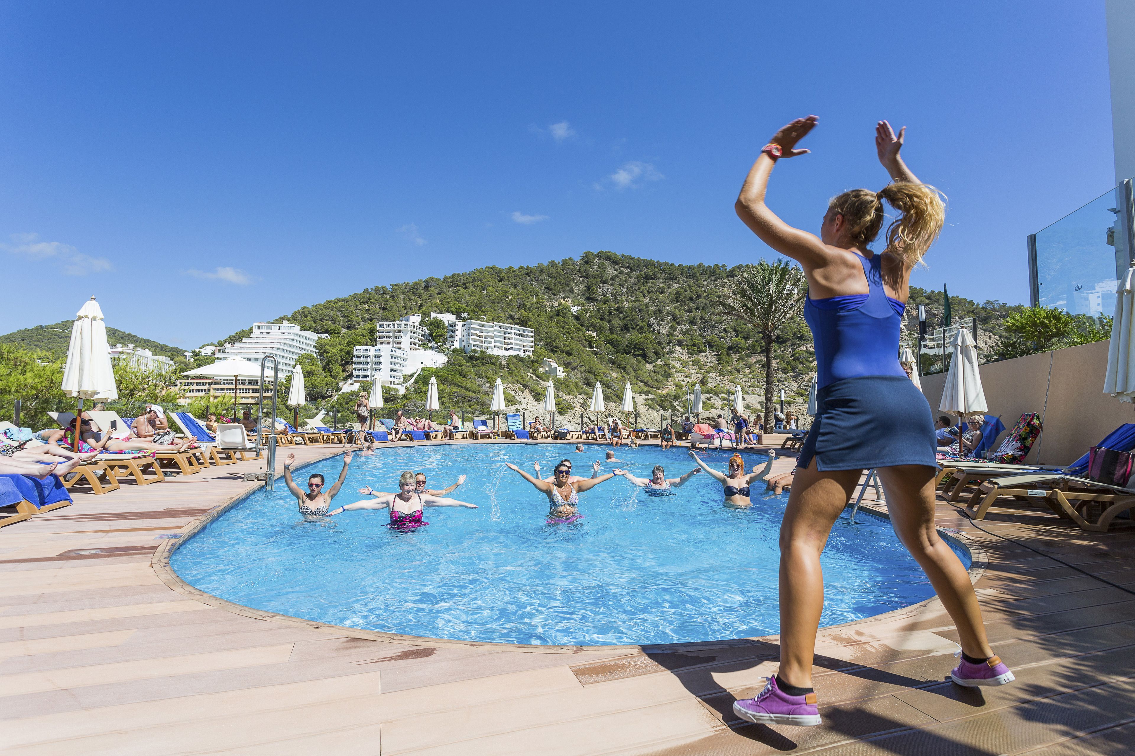 A swimming pool with people enjoying the water, surrounded by lounge chairs and umbrellas.