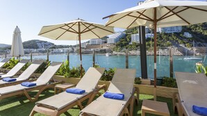 A seaside lounge area with sun loungers and umbrellas, overlooking a marina and coastal buildings. - Palladium Hotel Cala Llonga - Adults Only (Santa Eulalia del Rio)
