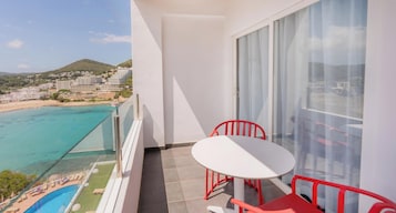 Un balcón con mesa y sillas, con vista a la playa y al paisaje urbano.