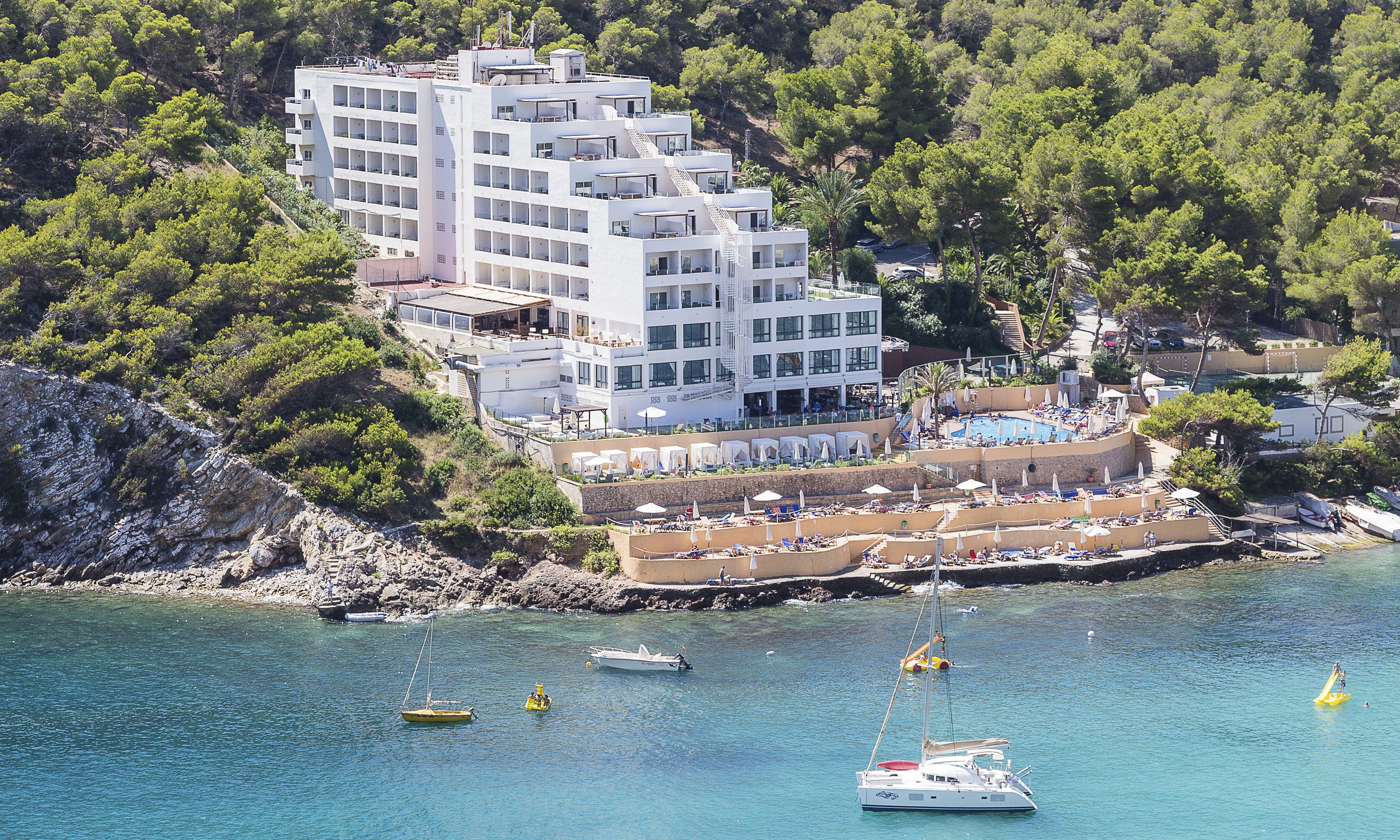 A coastal hotel with multiple balconies, a pool area, and boats in the water.