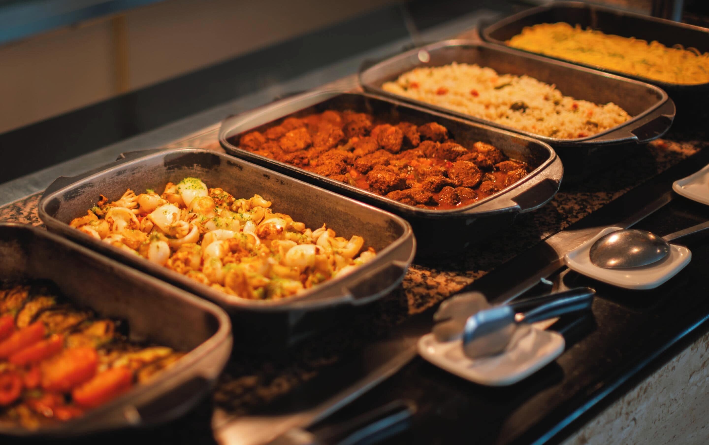 A buffet with various dishes in metal serving trays.