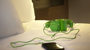 A hotel room with a bed, a green electronic device, and a smartphone on the bed. - ibis Styles Roanne Centre Gare (Roanne)