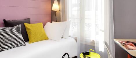 A hotel room with a bed, a bedside lamp, a small table with glasses, and a chair.