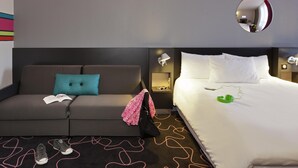 Habitación de hotel con cama, sofá, espejo, lámpara y alfombra de estampado ondulado.