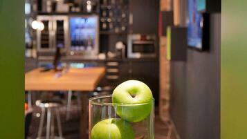 A modern kitchen with a dining area, a glass table with two apples, and a bar area with stools.