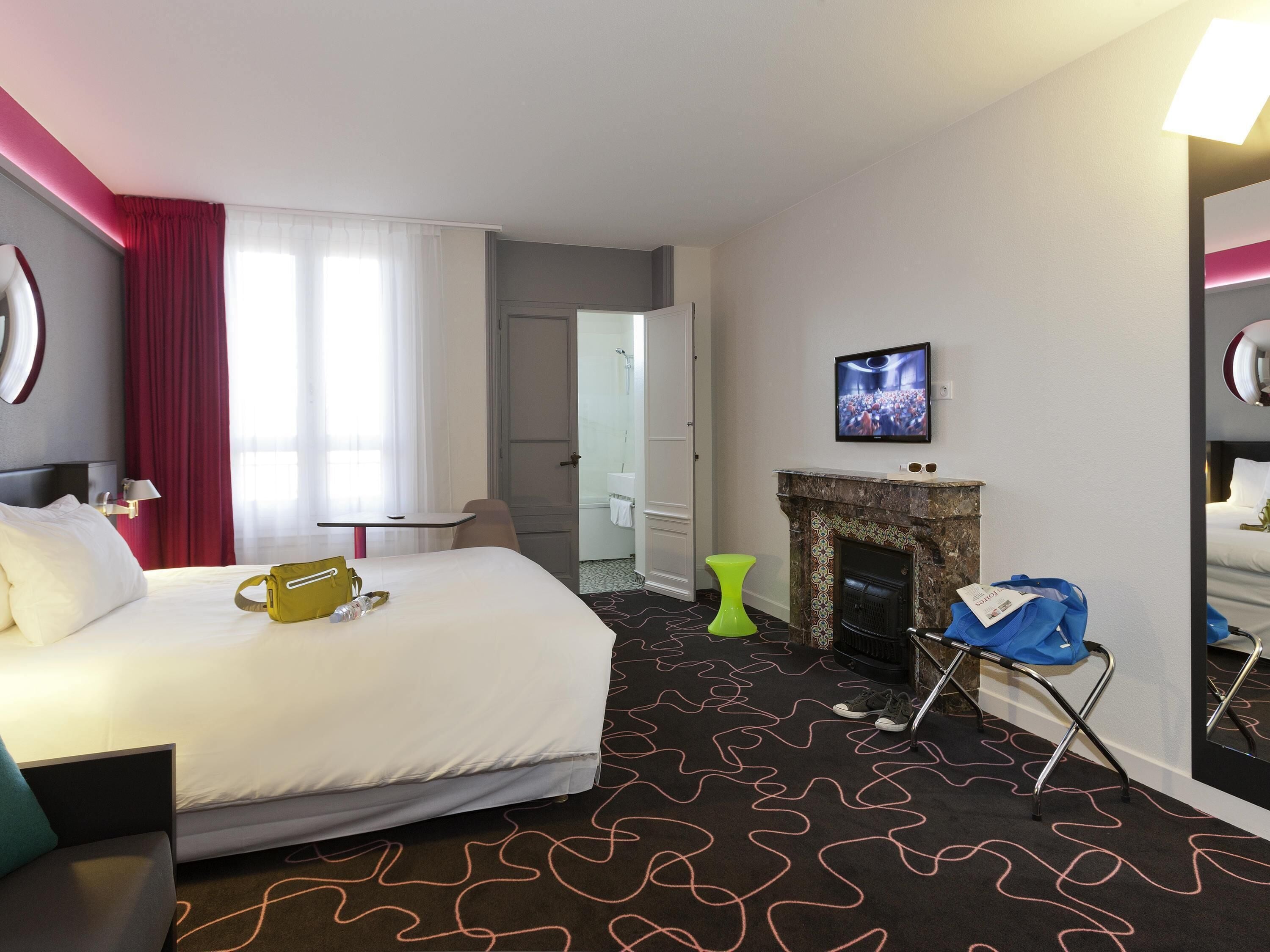 Una habitación de hotel con una cama, televisión, chimenea y puerta que da a un baño.
