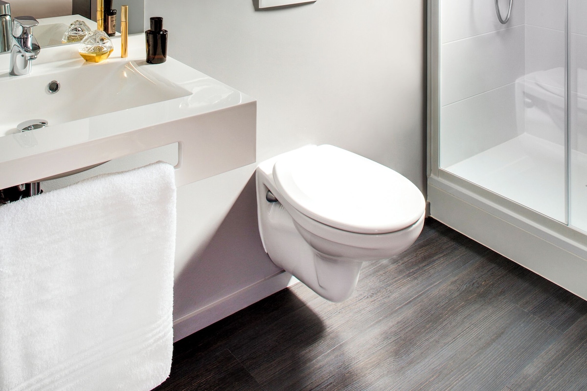 Un baño moderno con lavamanos, espejo e inodoro blancos.