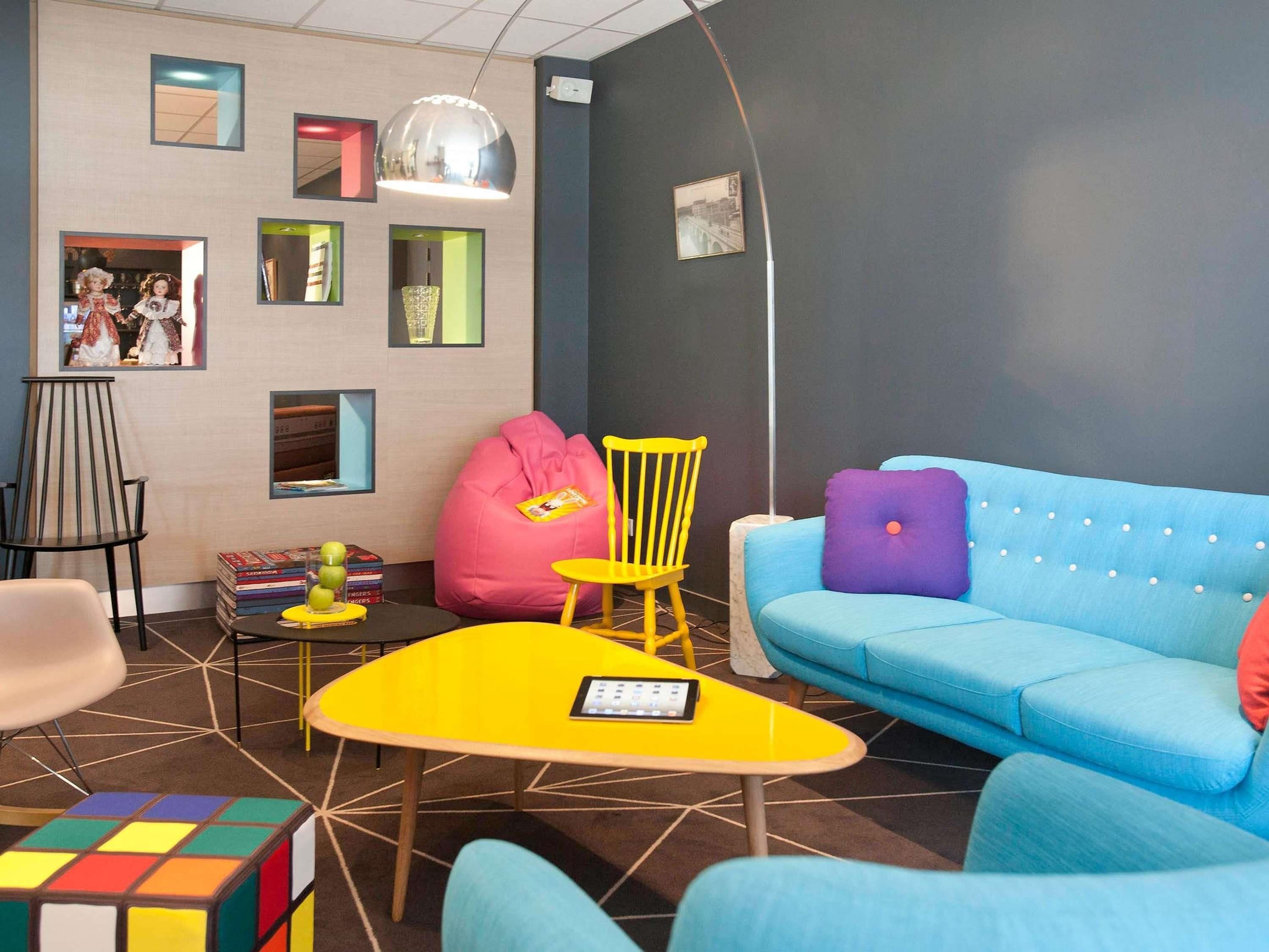 A modern living room with a blue sofa, yellow table, and colorful bean bag.