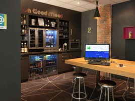 Una zona de bar con un monitor de ordenador, taburetes y estantes llenos de botellas.