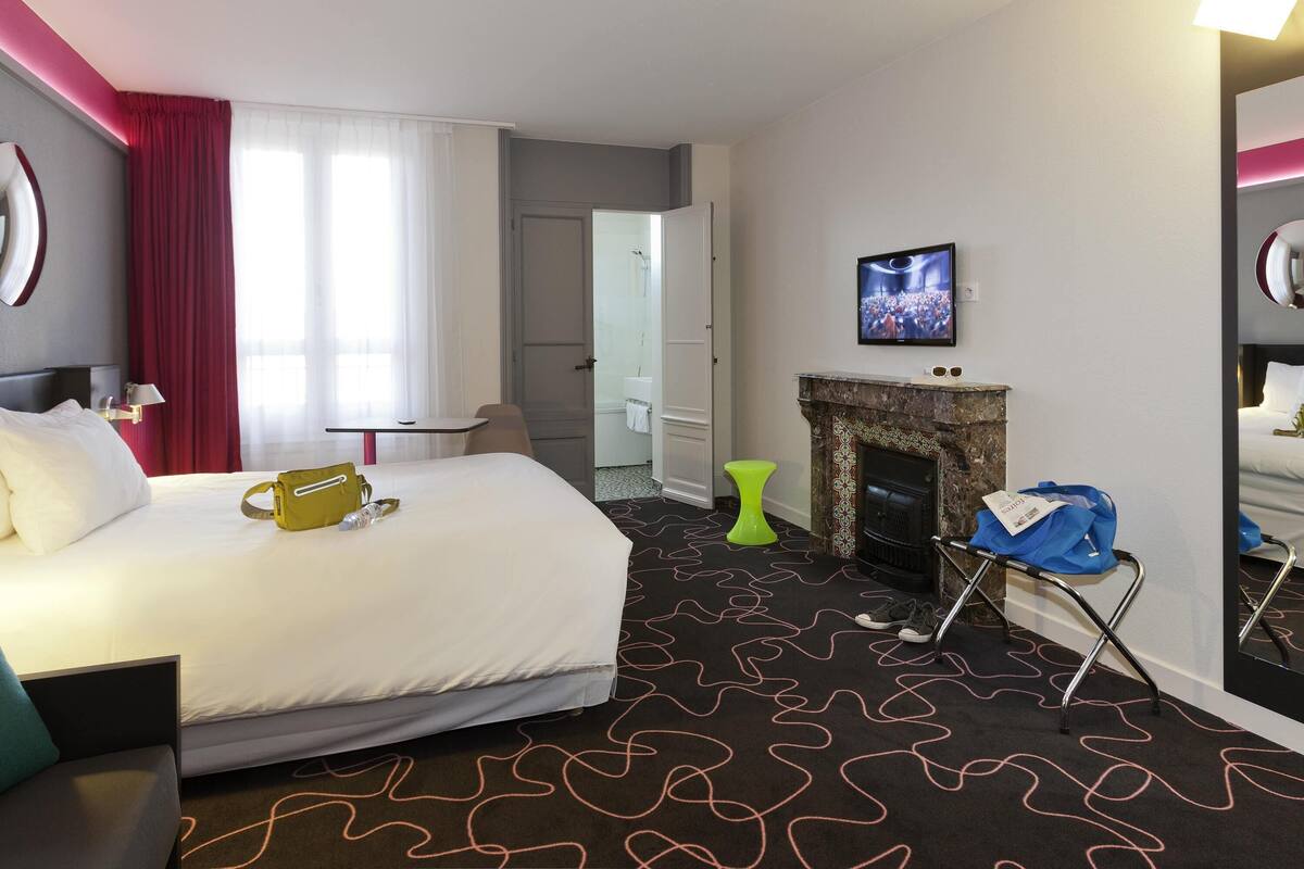 A hotel room with a bed, a television, a fireplace, and a door leading to a bathroom.