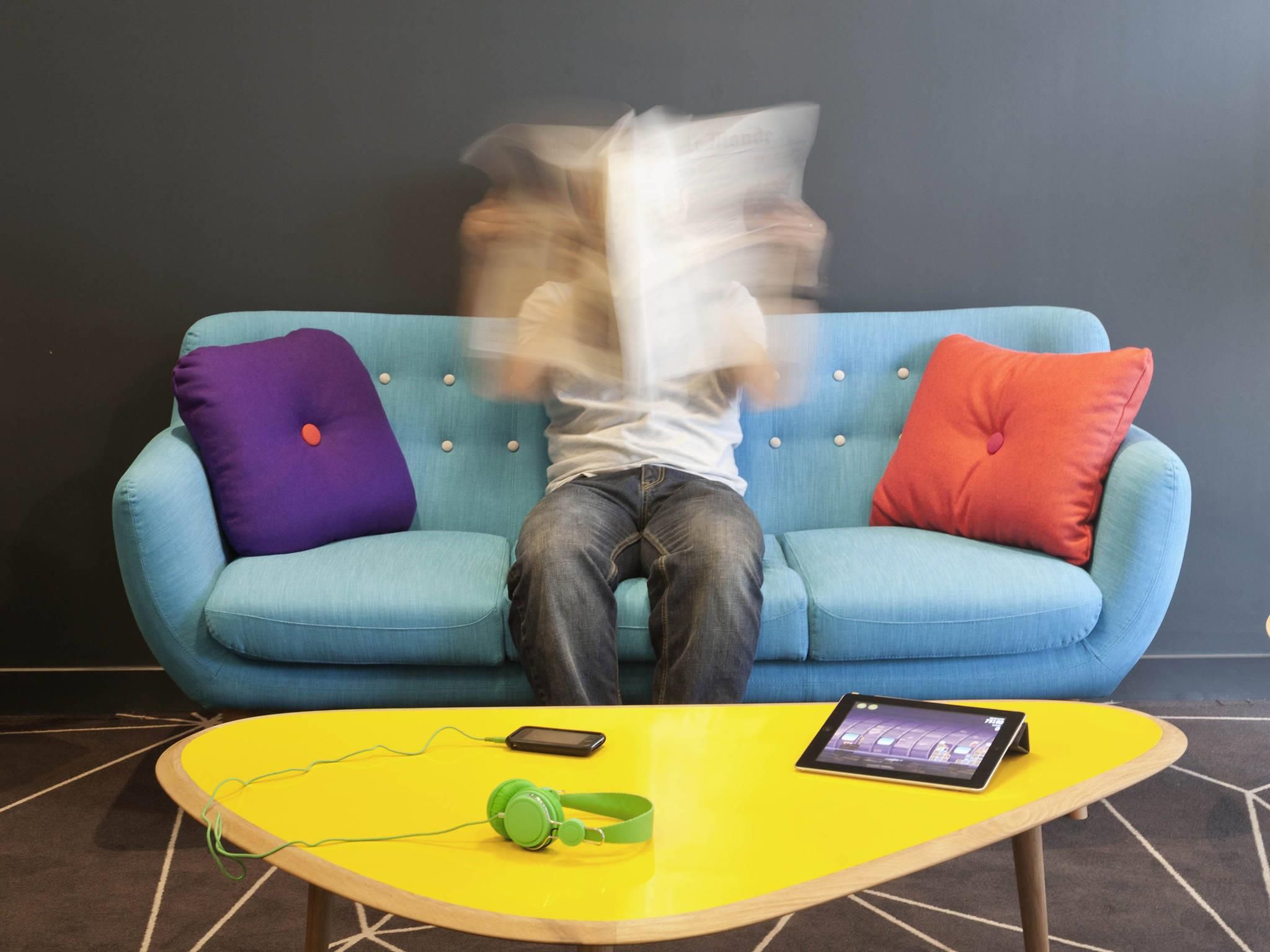 A person sitting on a blue sofa with a tablet and headphones on a yellow table.
