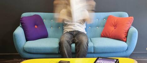 A person sitting on a blue sofa with a tablet and headphones on a yellow table.