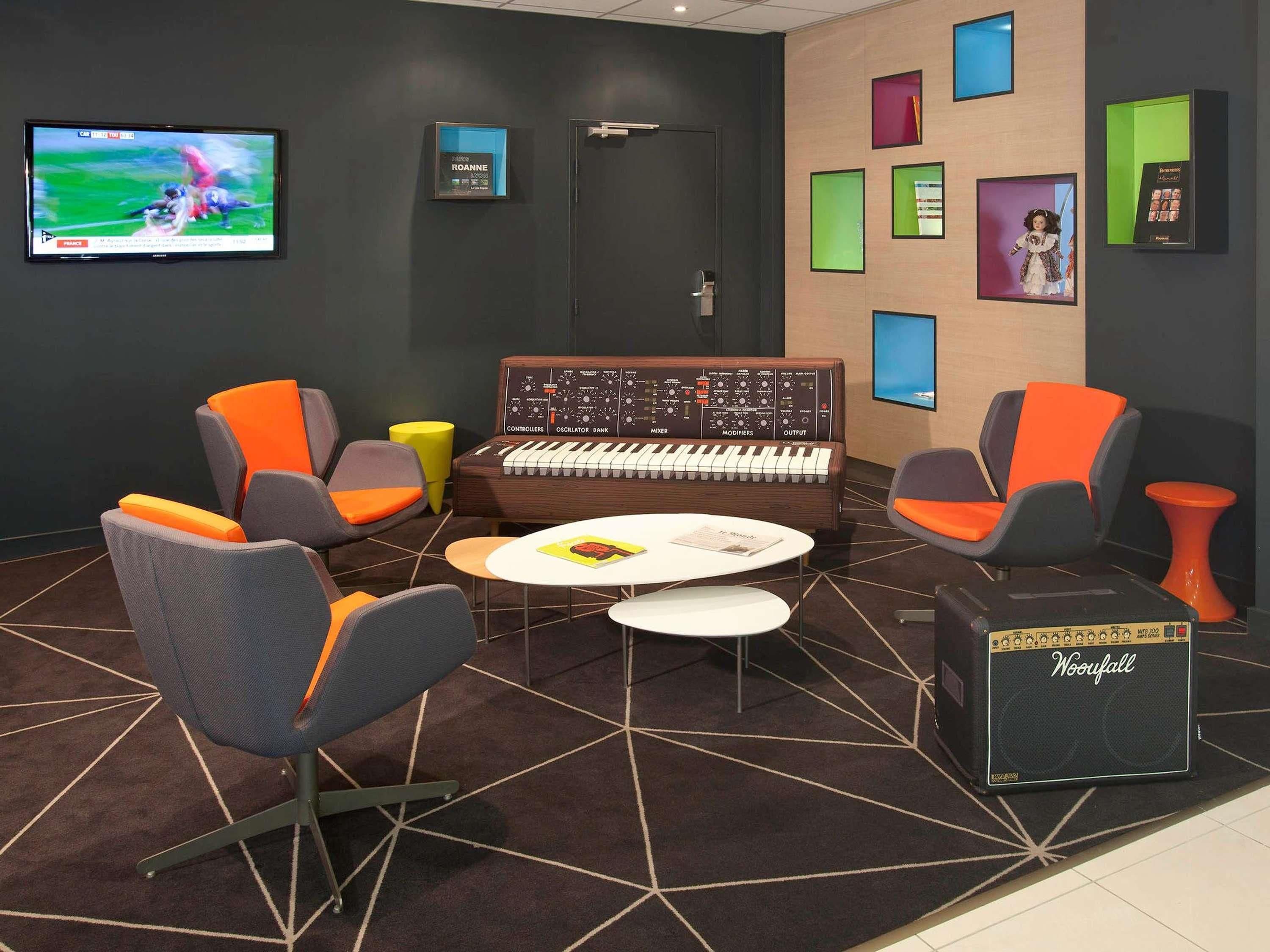 A lounge area with a small stage, a keyboard, a Woofall amplifier, and a television displaying a sports event.