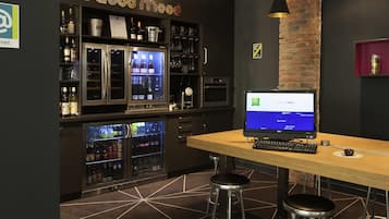 Una zona de bar con un monitor de computadora, taburetes y estantes llenos de botellas.