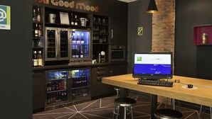 Zona de bar con computadora, taburetes y un refrigerador lleno de bebidas.