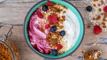 A bowl of yogurt with berries and granola on a wooden surface.